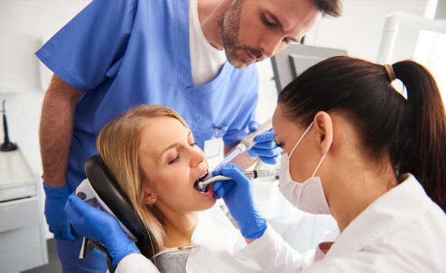 Stock image of a doctor performing tooth extraction to a patient accompanied by an assistant